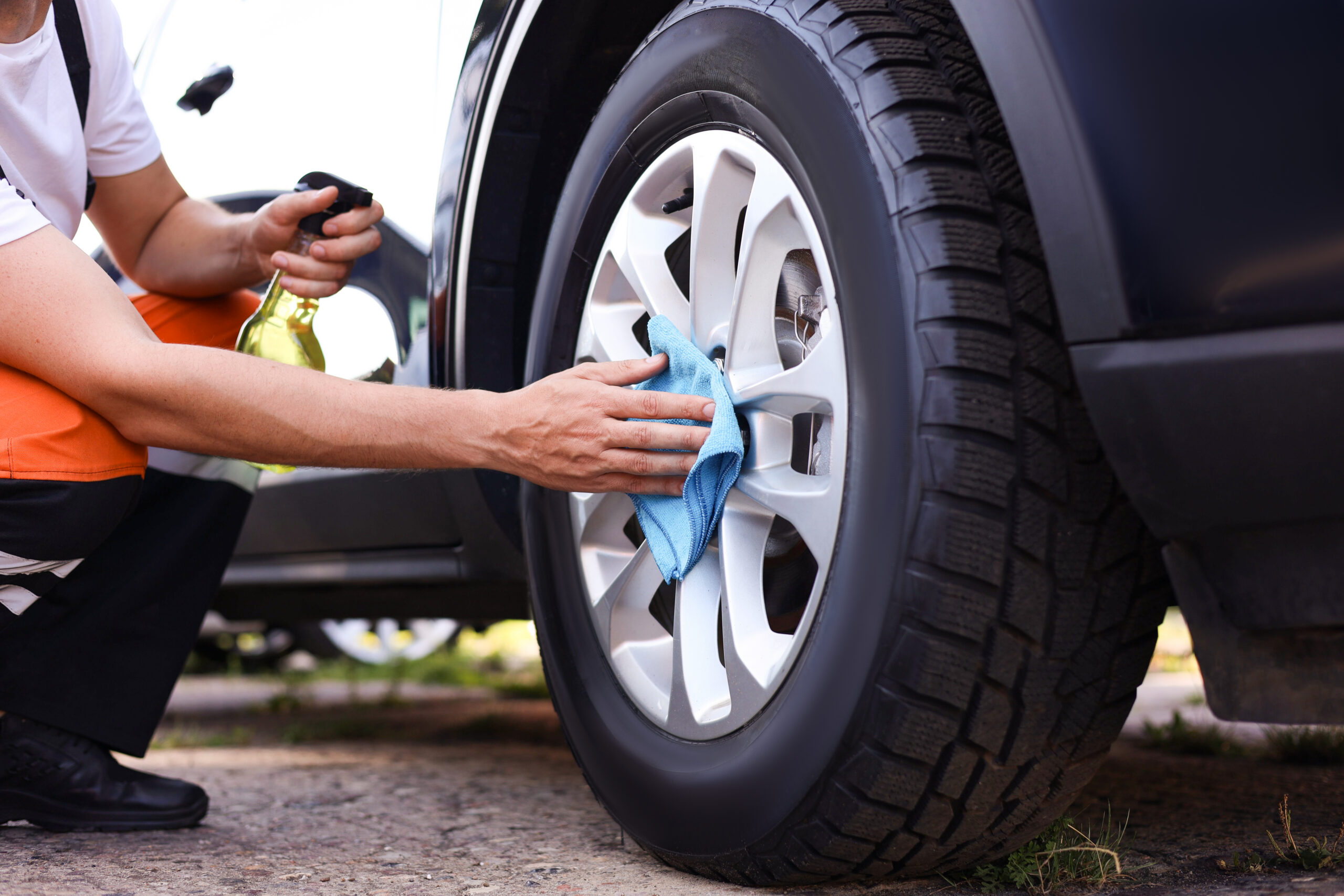 A person cleaning and detailing a vehicle wheel using a microfiber cloth and spray cleaner during spring vehicle maintenance. Malden Automotive in Amherstburg offers spring deals on car cleaning products including tire shine, detailing kits, microfiber towels, wash soaps, and interior cleaners.